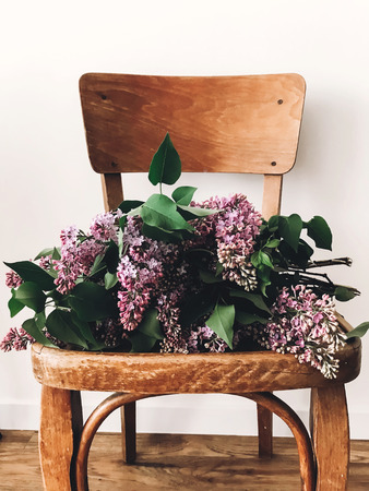 Stylish lilac purple bouquet on rustic wooden chair in room. Fresh spring lilac flowers bouquet on chair, countryside still life. Hello spring. Happy Mothers dayの写真素材