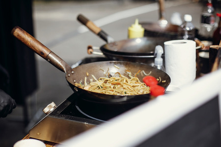 Asian street food festival in city. Chef cooking noodles and vegetables in a pan on fire. Fried chinese japanese noodles with vegetables and shrimps in wok on the open fireの写真素材