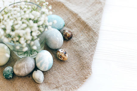Stylish Easter eggs  on rustic fabric with spring flowers on white wooden background, flat lay with space for text. Modern colorful easter eggs painted with natural dye. Happy Easterの写真素材
