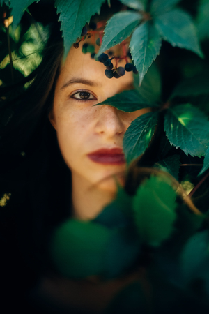 Stylish hipster girl posing at green leaves, atmospheric moment. Portrait of fashionable cool woman relaxing in park. Selective focus, creative retro image. Space for textの写真素材