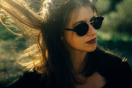 Stylish hipster girl posing in sunny park with amazing sun beams, atmospheric moment. Fashionable woman portrait in sunglasses in evening. Selective focus. Retro effect. Creative imageの写真素材