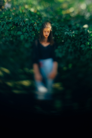 Stylish hipster girl posing at green leaves bush, atmospheric moment. Fashionable woman in denim...