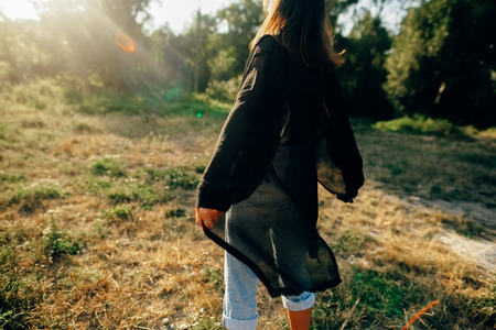 Stylish hipster girl having fun in sunny park in amazing sunbeams, atmospheric moment. Fashionable cool woman dancing in evening light, back view. Selective focus. Retro effect. Creative imageの写真素材
