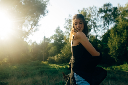 Stylish hipster girl having fun in sunny park in amazing sunbeams, atmospheric moment. Fashionable cool woman dancing and smiling in evening light. Selective focus. Retro effect. Creative imageの写真素材
