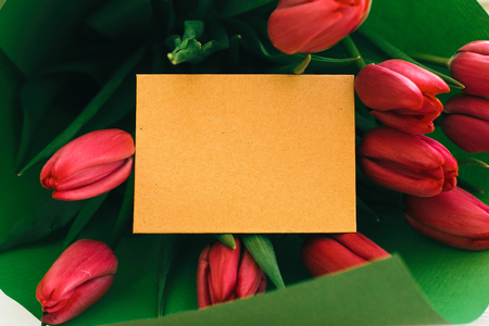 Beautiful red tulips bouquet in green paper and craft card with space for text on white wooden background. Happy mothers day.  Greeting card template. Valentines day. Pink tulips on white woodの写真素材
