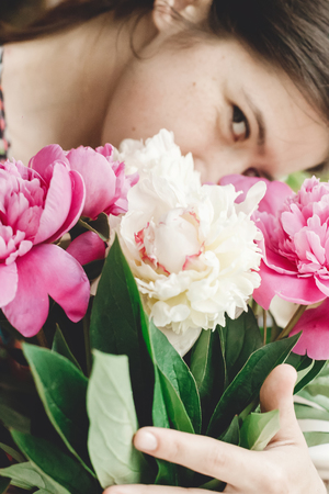 Girl holding and smelling beautiful pink and white peonies bouquet at rustic old wooden window. Floral decor and arrangement. Gathering flowers. Rural still life, countrysideの写真素材