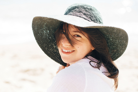Happy young boho woman in hat relaxing and enjoying sunny warm day at ocean. Space for text. Stylish hipster girl sitting on beach and tanning. Summer vacation. Calm emotionsの写真素材