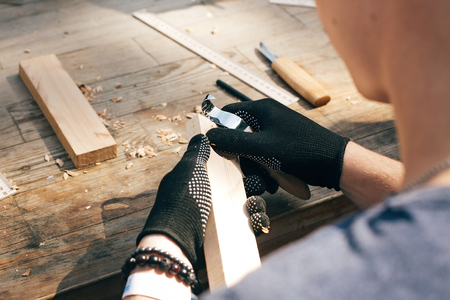 Wooden workshop. Hands carving spoon from wood, working with chisel close up. Process of making wooden spoon, chisel, pencil, compass, ruler on dirty table with shavingsの写真素材