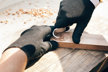 Wooden workshop. Hands carving spoon from wood, working with chisel close up. Process of making wooden spoon, chisel, pencil, compass, ruler on dirty table with shavingsの写真素材