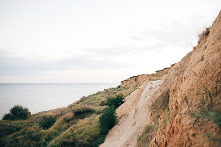 Beautiful sandy cliff with grass and ground path to calm sea. Beach  on tropical island at ocean bay or lagoon. Tranquil calm moment. Summer vacation. Copy spaceの写真素材