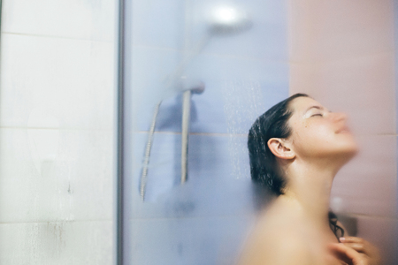 Young happy woman taking shower at home or hotel bathroom. Beautiful  brunette girl washing her hair and enjoying relax time. Body and skin hygiene, lifestyle conceptの写真素材