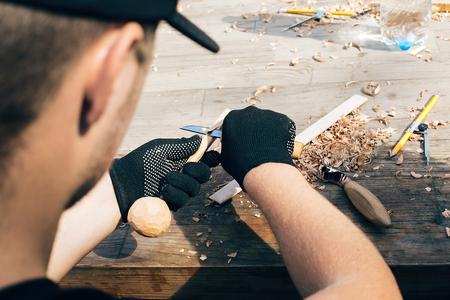 Hands carving spoon from wood, working with chisel close up. Wooden workshop. Process of making...