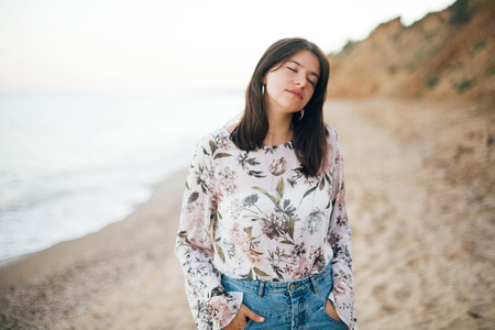Stylish hipster girl walking on beach at sea. Calm portrait of happy fashionable boho woman relaxing at sandy cliff on tropical island. Travel and summer vacation. Space for textの写真素材