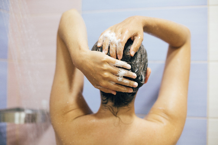 Young happy woman washing her hair with shampoo, hands with foam closeup. Back of beautiful brunette girl taking shower and enjoying relax time. Body and hair hygiene, lifestyle conceptの写真素材