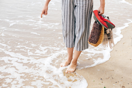 Girl trying to write summer word or sun symbol  on sandy beach at sea, but waves ruins the sign....