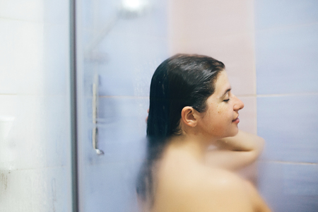 Young happy woman taking hot shower at home or hotel bathroom. Sensual portrait of beautiful brunette girl enjoying time in shower. Body and skin hygiene, lifestyle concept. Space textの写真素材