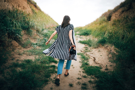 Stylish hipster girl running on sandy cliff  to sea and holding photo camera.  Happy young boho woman exploring tropical island at sandy cliff beach. Summer vacation. Space for text.の写真素材
