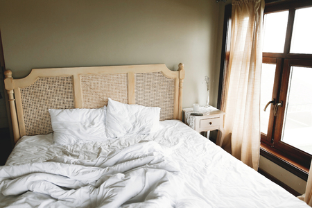 Bed with white sheets and vintage nightstand with decor at window  in hotel room or provence home bedroom. Space for text. Enjoying morning conceptの写真素材