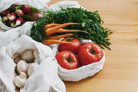 Zero waste grocery shopping concept. Reusable eco cotton bags with fresh vegetables carrots,tomatoes, arugula, mushrooms from market on wooden table. ban plastic. Sustainable lifestyle.の写真素材