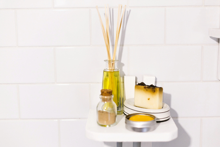 Zero waste bathroom concept. Eco natural shampoo in metal can,  fragrance oil, soap and ayurveda ubtan powder in glass on wooden shelf in bathroom, plastic free items. Sustainable lifestyleの写真素材