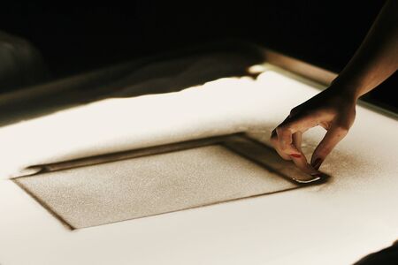 Sand animation at wedding reception. Hand drawing on sand on light box in dark room, creative sand show. Person painting on sandの写真素材