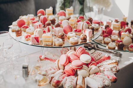Delicious pink candy bar at wedding reception. Pink and white desserts,macarons and cupcakes on stand, modern sweet table at wedding or baby shower. Luxury catering conceptの写真素材