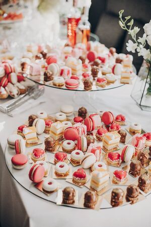 Delicious pink candy bar at wedding reception. Pink and white desserts,macarons and cupcakes on stand, modern sweet table at wedding or baby shower. Luxury catering conceptの写真素材