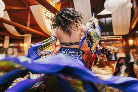 Beautiful gypsy girls dancing in traditional blue floral dress at wedding reception in restaurant. Woman performing romany dance and folk songs in national clothing. Roma gypsy festivalの写真素材
