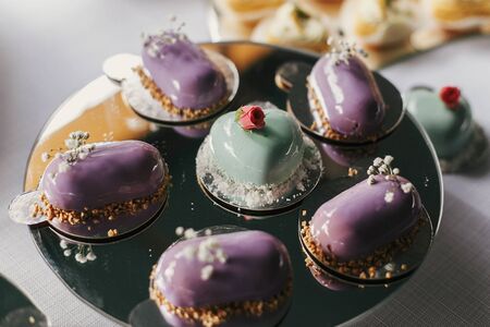Colorful eclairs, heart shape cream desserts on stand, modern sweet table at wedding or baby shower....