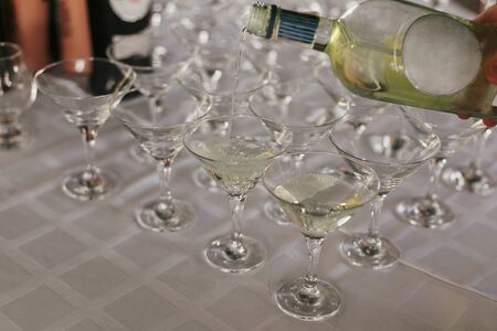 Waiter pouring martini drink in glass on table at wedding reception. Row of glasses for martini, alcohol bar at wedding or christmas feast. Luxury catering concept.の写真素材