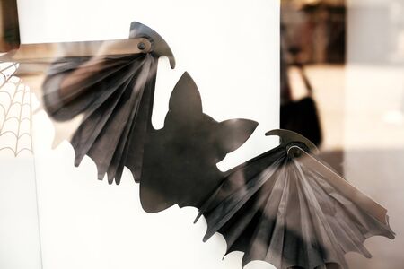Flying scary bat and spider web on window in city street, holiday decoration of store fronts....