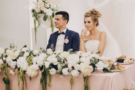 Stylish bride and groom sitting together at beautiful pink centerpiece decorated with flowers at...