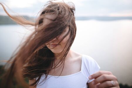 Portrait of hipster girl with windy hair standing on top of rock mountain with beautiful sunset view on river. Atmospheric tranquil and calm moment. Copy space.の写真素材
