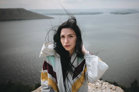 Stylish hipster girl with windy hair sitting on top of rock mountain with beautiful view on river....