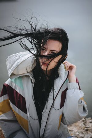 Stylish hipster girl with windy hair sitting on top of rock mountain with beautiful view on river....