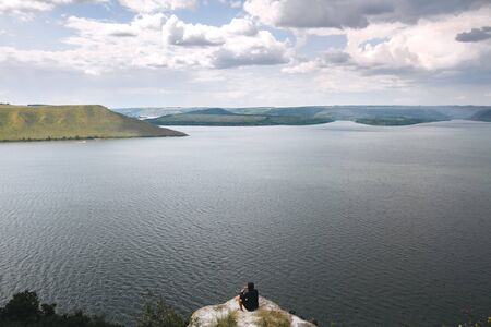 Stylish hipster traveler sitting on top of rock mountain with amazing view on river. Young guy...