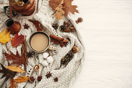 Autumn flat lay, cozy inspirational image.Hygge lifestyle. Coffee cup with  fall leaves, anise,herbs, acorns, nuts , cinnamon, cotton on white knitted sweater. Autumn mood.の写真素材