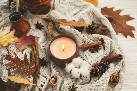 Hygge lifestyle. Candle with berries, fall leaves, anise,herbs, acorns, nuts , cinnamon, cotton on white knitted sweater. Autumn mood. Hello autumn, cozy inspirational imageの写真素材