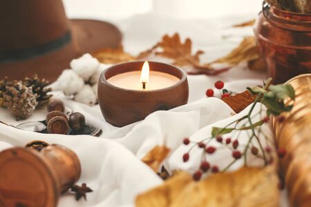 Autumn mood. Candle, berries, fall leaves, herbs, acorns, nuts and brown hat on white fabric. Hello autumn, cozy inspirational image. Hygge lifestyleの写真素材