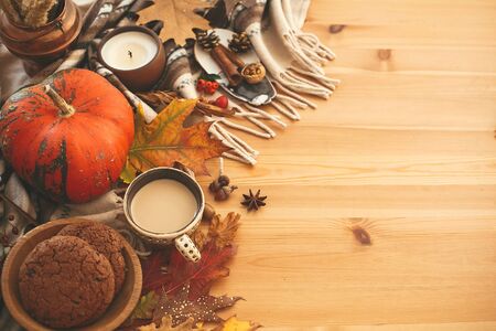 Coffee cup, candle,pumpkins with berries, fall leaves, anise,herbs, acorns, nuts, cinnamon, cotton on brown blanket, flat lay. Hygge lifestyle, cozy autumn mood.の写真素材