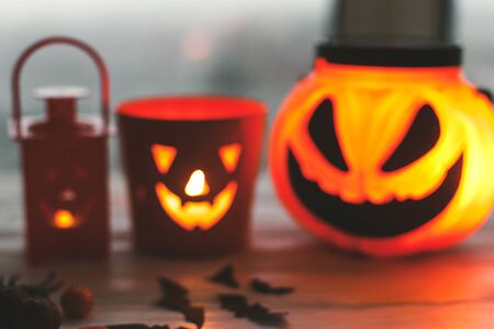 Blurred image of glowing jack o lantern face, festive candy, skulls, black bats, ghost, spider decorations on white woodenの写真素材