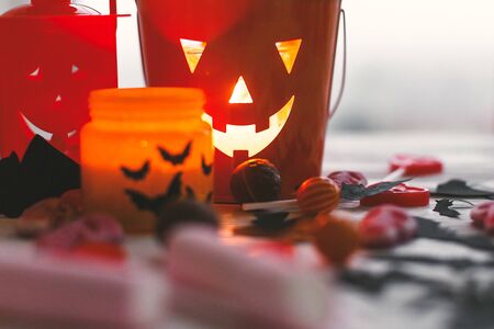 Halloween jack o lantern bucket, glowing candle, festive candy, skulls, black bats, ghost, spider decorations on white woodenの写真素材