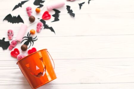 Trick or treat. Halloween candy spilled from jack o lantern bucket with skulls, black bats, ghost, spider decorations on white woodenの写真素材