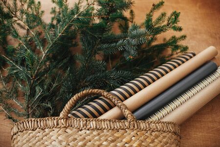 Rustic basket with fir branches and festive wrapping paper on rustic wooden background. Winter holiday preparations. Slow living lifestyle. Christmas tree branches in straw bagの写真素材
