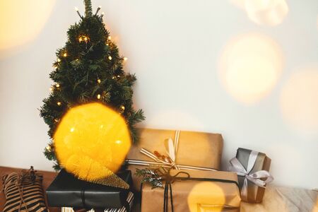 Christmas tree with festive stylish gifts in golden lights bokeh in white room. Merry Christmas.Winter holidays preparation. Copy space. Happy Holidays. Season's Greetingの写真素材