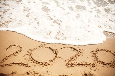 Happy New Year 2020, handwritten on sandy beach. 2020 numbers inscription on golden sand and waves foam at sea beach. Tropical celebrationの写真素材