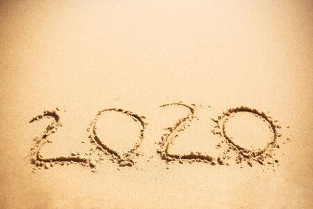 Happy New Year 2020, handwritten on sandy beach. 2020 numbers inscription on golden sand at sea beach. Tropical celebration.の写真素材