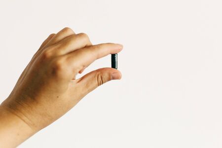 Dietary supplements. Hand holding spirulina capsule on white wall background. Morning vitamin...