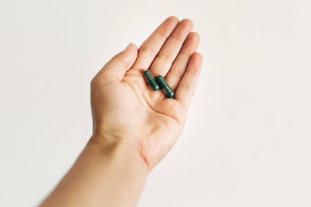 Dietary supplements. Hand holding spirulina capsules on white wall background. Morning vitamin nutrient pill. Health support and treatment. Biologically active additivesの写真素材