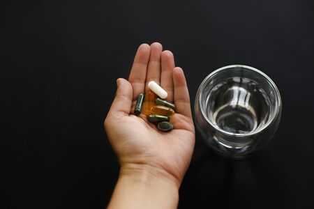 Dietary supplements. Hand holding omega 3, spirulina, chlorophyll,magnesium  capsules above glass of water. Morning dose of pills. Health support. Biologically active additivesの写真素材